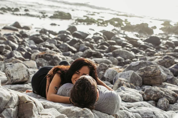 Tattooed woman and man lying together on rocky beach near ocean — Stock Photo