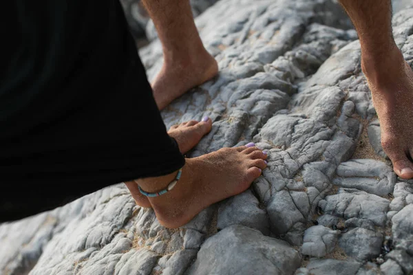 Cropped view of barefoot woman with ankle bracelet and man standing on rocks — Stock Photo
