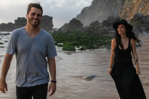 Tattooed woman in hat looking at bearded man smiling and walking in ocean water — Stock Photo