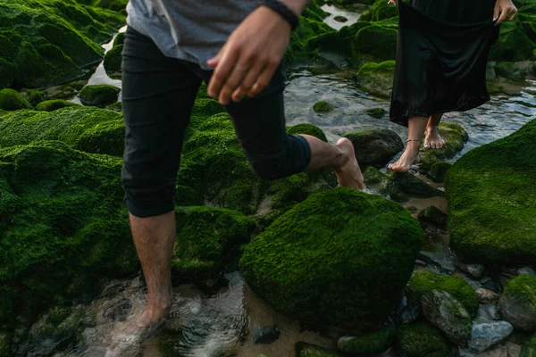 Cropped view of couple walking near green mossy stones in ocean — Stock Photo