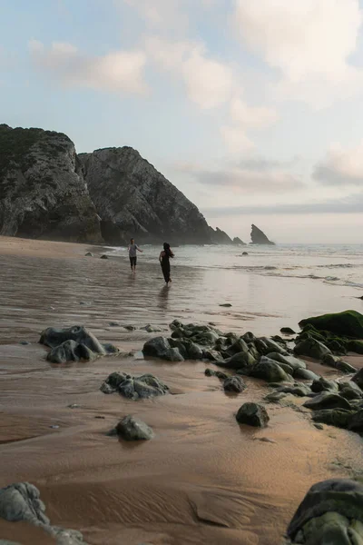 Happy man with outstretched hands meeting girlfriend in hat and dress walking on wet sand in ocean — Stock Photo