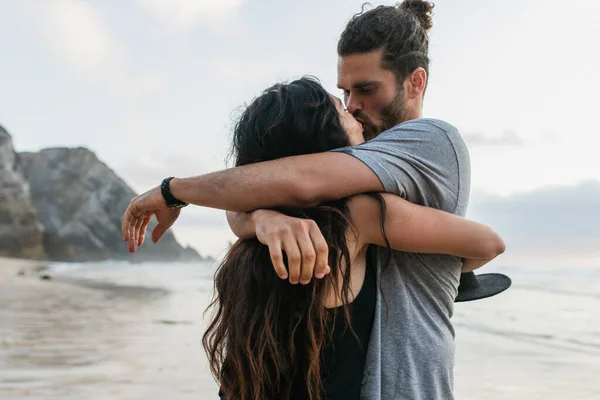 Homme barbu et femme brune étreignant et embrassant sur la plage en portugais — Photo de stock