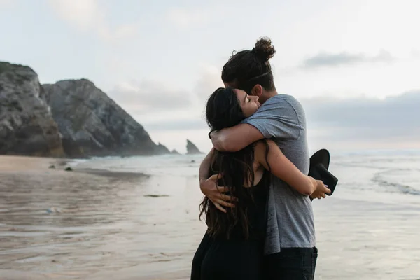 Homme et femme brune tenant chapeau et étreinte sur la plage en portugais — Photo de stock