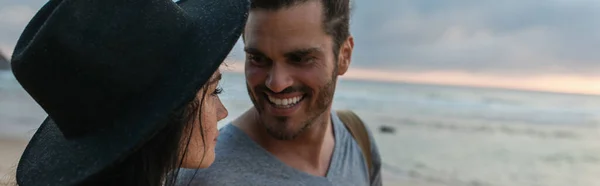 Homme barbu joyeux regardant femme en chapeau noir sur la plage, bannière — Photo de stock