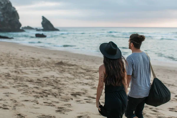 Vista trasera de la mujer tatuada y el hombre caminando juntos en la playa de arena - foto de stock