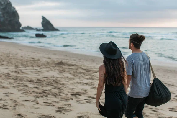 Rückansicht tätowierter Frau und Mann, die gemeinsam am Sandstrand spazieren gehen — Stockfoto