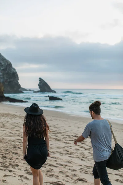 Вид на татуированную женщину и бородатого мужчину с сумкой, идущего вместе по песчаному пляжу — стоковое фото