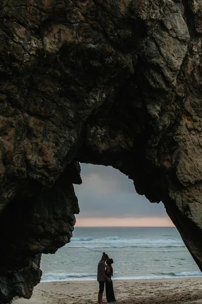 Вид сбоку пары, обнимающейся, стоя на пляже во время заката — стоковое фото