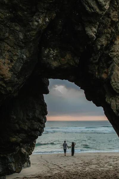 Вид сзади пары, держащейся за руки, стоя на пляже во время заката — стоковое фото