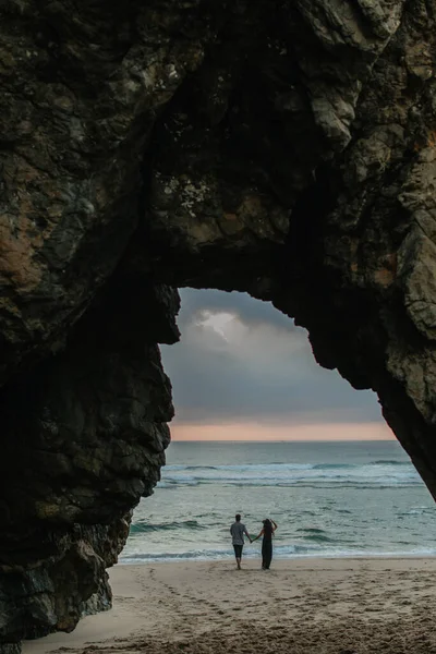 Rückansicht eines Paares, das sich Händchen hält, während es am Strand bei Sonnenuntergang steht — Stockfoto