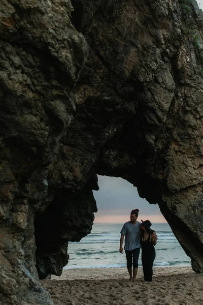 Bearded man and woman in dress walking on sandy beach near ocean during sunset — Stock Photo