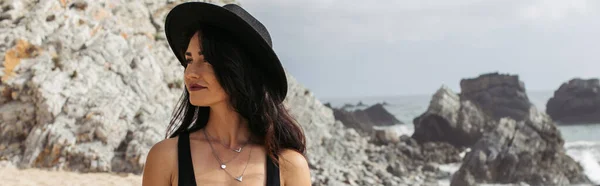 Femme en chapeau noir debout sur la plage près de l'océan en portugais, bannière — Photo de stock