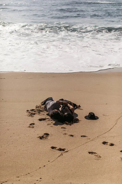 Pareja abrazo y acostado en mojado arena cerca de océano en playa - foto de stock
