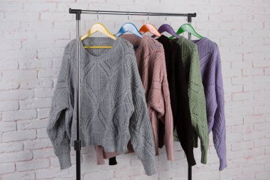 Askılarda asılı beş renkli yün kazak, beyaz tuğla duvar zeminine karşı, çeşitlilik kavramı