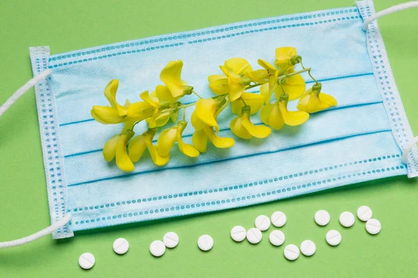 緑の背景に青い医療用マスクマスク黄色の花序の横に散在する白い錠剤コンセプトアレルギーコピースペース — ストック写真