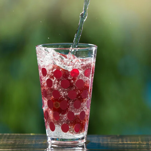 soda water pouring into a glass cup with strawberries illuminating the drink against a background of greenery