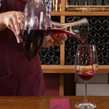 Kadın eli şarap sürahisini tutuyor, bardağa şarap dolduruyor, tadımlık konsept yapıyor.