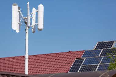 Evin çatısındaki rüzgar jeneratörü ve güneş panelleri temiz yenilenebilir enerji, yakın plan, mavi gökyüzüne karşı.