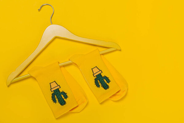 pair of socks with cacti on a wooden hanger, on a yellow background, concept of sales and discounts, copy space