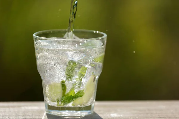 a glass with ice cubes, with lime and with mint, soda water from the bottle, in the open space, sunlight and bokeh, concept