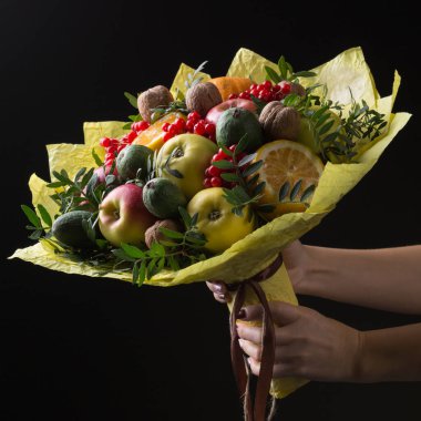 Kadınların elinde, siyah bir arka planda, sağlıklı yiyecek kavramı olan, kağıda sarılmış, sebze, meyve ve fındık gibi gastronomik bir set vardır.
