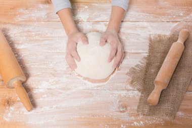 Hamur yoğurup tahta bir tahtanın üzerinde yuvarlanan bir kızın elleri.