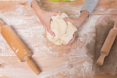 Hamur yoğurup tahta bir tahtanın üzerinde yuvarlanan bir kızın elleri.