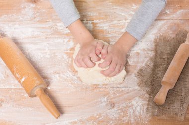 Hamur yoğurup tahta bir tahtanın üzerinde yuvarlanan bir kızın elleri.