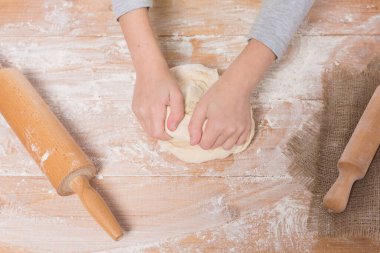 Hamur yoğurup tahta bir tahtanın üzerinde yuvarlanan bir kızın elleri.