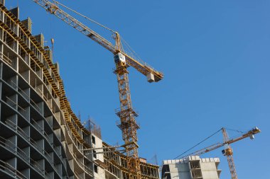 İnşaat halindeki evin yakınından geçen iki sarı vinç, evin iskeleti ve vinç parçaları.