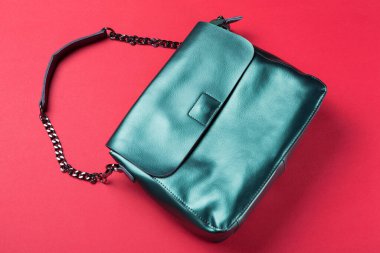 Uzun saplı turkuaz kadın çantası. Kırmızı arka planda bir zincir.