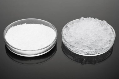 Hidro-jel tozu ve jöle gibi, sudan şişmiş, büyük cam parçaları koyu bir yüzeyde, yakın plan.