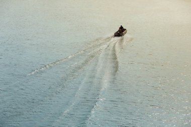 İki adam yüksek hızda bir motorlu teknede, suda izler var, oltayla balık avlamaya gidiyorlar.