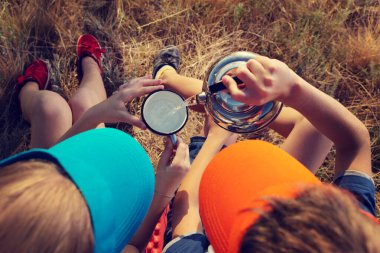 Kız ve oğlan yürüyüş yapıyor, çimenlere oturuyor ve su içiyor, oğlan bardağa su dolduruyor, üst manzara.
