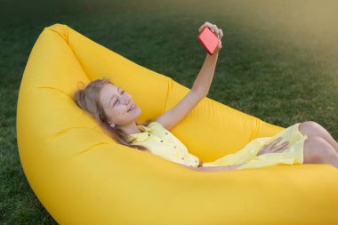 Mutlu kız doğada dinleniyor, şişme bir kanepeye uzanıyor ve selfie çekiyor, yaşam tarzı.