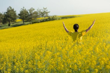 Sarı ceketli, çiçekli kanola tarlasında bir kadın doğaya sarılıyor.