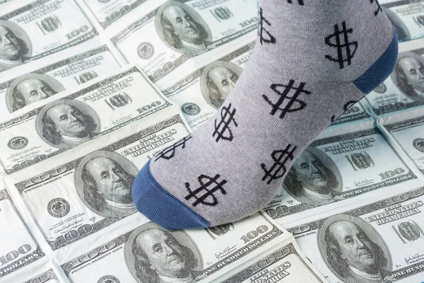 foot in a sock with the image of the dollar symbol, stands on spread out dollars, the concept of financing