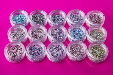 Pembe arka planda tırnakları için çok renkli kıvılcımları olan akrilik kavanozlar, seçici odaklanma