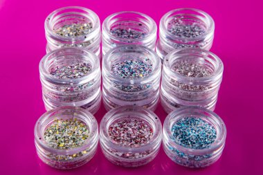 Pembe arka planda tırnakları için çok renkli kıvılcımları olan akrilik kavanozlar, seçici odaklanma