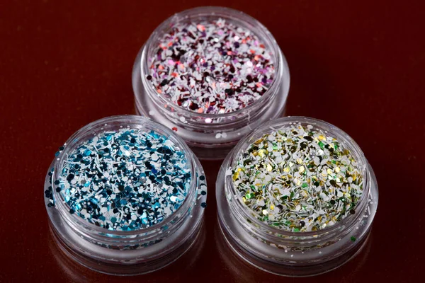 Koyu kırmızı arka planda tırnakları için çok renkli kıvılcımları olan üç akrilik kavanoz.