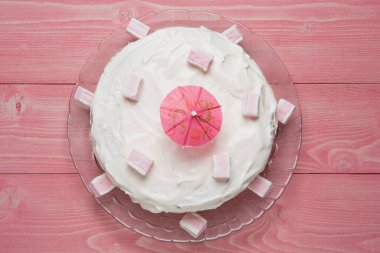 ballı pasta ekşi kremayla kaplı, pembe tahta tahtalarda, marşmelovlarla süslenmiş, üst manzara