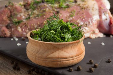 Dilimlenmiş yeşil baharatlar, maydanoz ve dereotu, ahşap bir kasede, çiğ hindi etinin arka planında