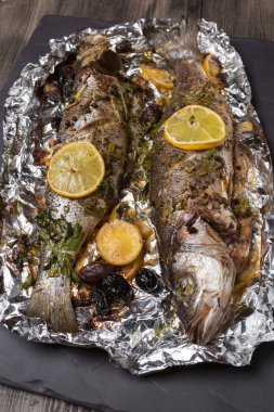 Fırında ya da ızgarada pişmiş iki deniz kabuğu balığı, besin folyosunda, siyah levhada