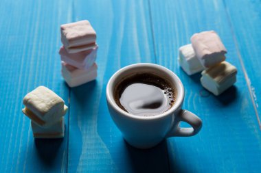 Etrafı marşmelovlarla çevrili mavi tahtalarda bir fincan sade kahve.