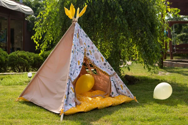 empty tepee-like children's tent outdoors, surrounded by balloons, children's party