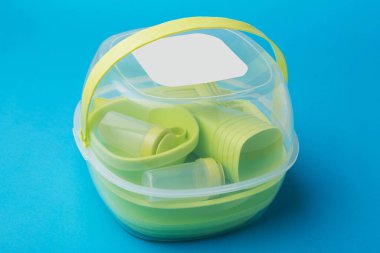 Konteynırdaki plastik tabaklar, yeşil yeniden kullanılabilir kaplar, set üst üste dizilmiş, mavi arka planda.