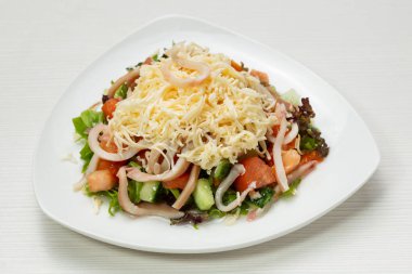 Taze sebze ve sebze salatası, mürekkep balığı halkaları ve peynirli, masada, beyaz bir tabakta.