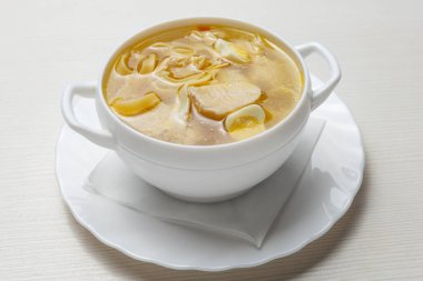 Erişte çorbası, et ve bıldırcın yumurtaları, beyaz tabakta, masanın üstünde.