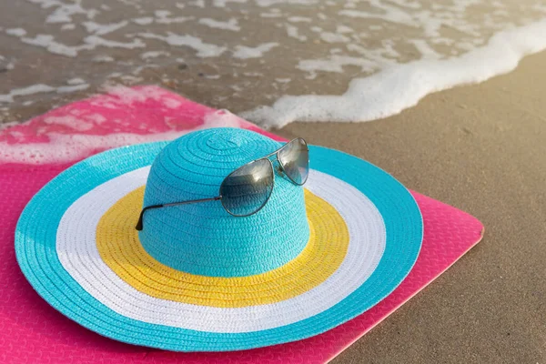 minimal concept of a beach trip, colorful hat on the beach near the water, on a pink fitness mat, close-up