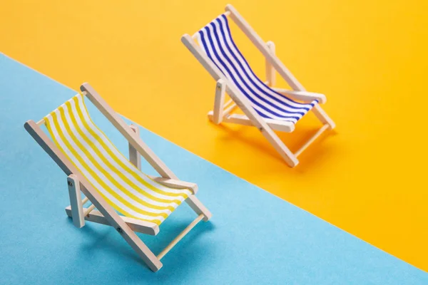 two lounge chairs stand on a blue and yellow background, minimal concept of vacation and summer